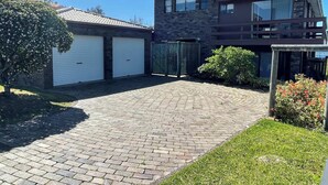 A two-story house with a garage, a paved driveway, and a small garden area. - Stunning Clifftop Location (Mollymook Beach)