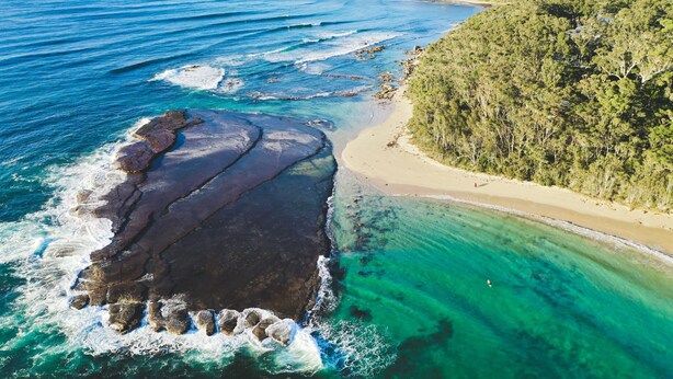 An aerial view of a coastal area with clear waters, a sandy beach, and a forested hill. - Stunning Clifftop Location (Mollymook Beach)