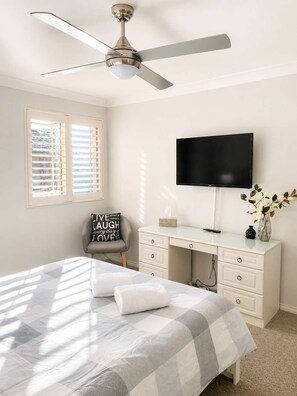 A bedroom with a bed, a desk, a chair, a ceiling fan, a TV, and a window with blinds. - Perfect Location Near Collers Beach (Mollymook)