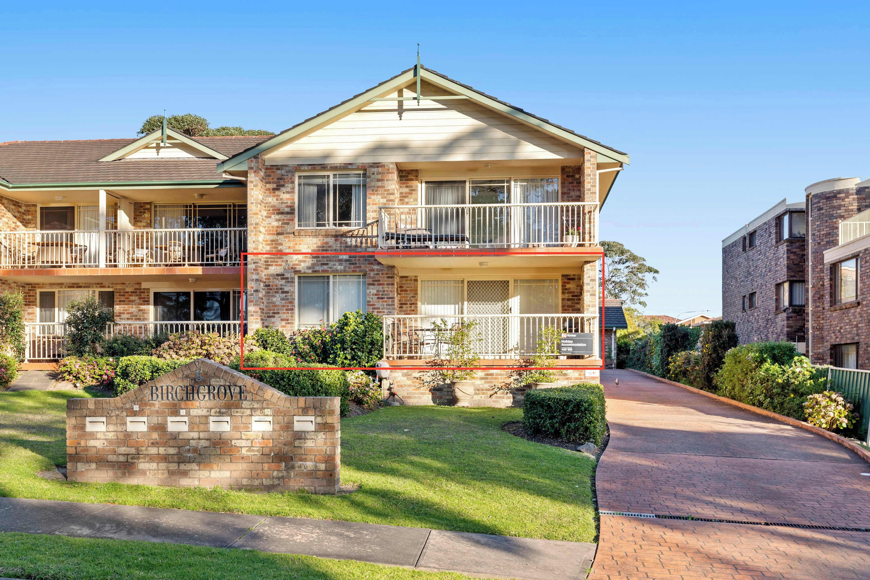 A two-story brick building with a balcony, a driveway, and a well-maintained lawn.