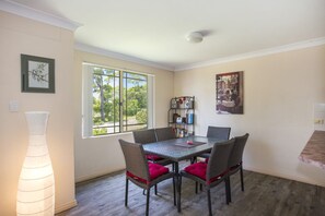 Un coin repas avec une table et des chaises, une bibliothèque et une fenêtre donnant sur les arbres.