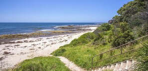 A coastal path leading to a beach with a clear view of the ocean and a rocky outcrop with vegetation.