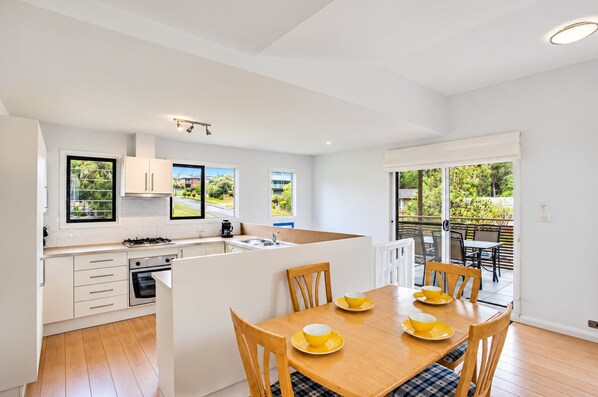 A modern kitchen with a central island, a dining area with yellow tableware, and a view of greenery through the windows.