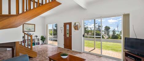 A spacious living room with a wooden staircase, a television, and a large sliding glass door leading to a patio.