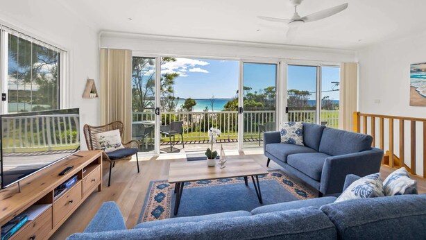 A spacious living room with a large sliding glass door leading to a balcony, a ceiling fan, and a view of the ocean. - Seaside Beach House (Dolphin Point)