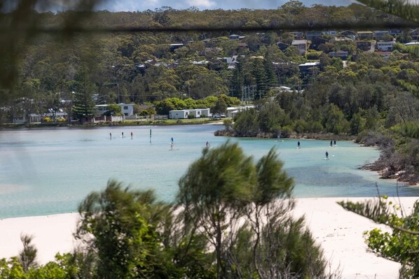 A coastal area with a sandy beach, clear blue water, and houses in the background. - Seaside Beach House (Dolphin Point)