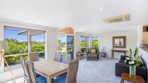 Relax in a spacious living area with a large dining table and comfortable seating, surrounded by expansive views of lush greenery.