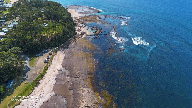 Vista aérea de una zona costera con playa, costa rocosa y un campo de golf.