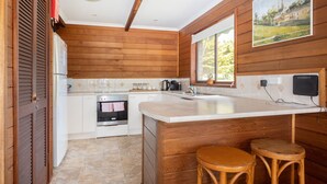 Una cocina con paneles de madera, una encimera blanca, un fregadero, una estufa y dos taburetes.