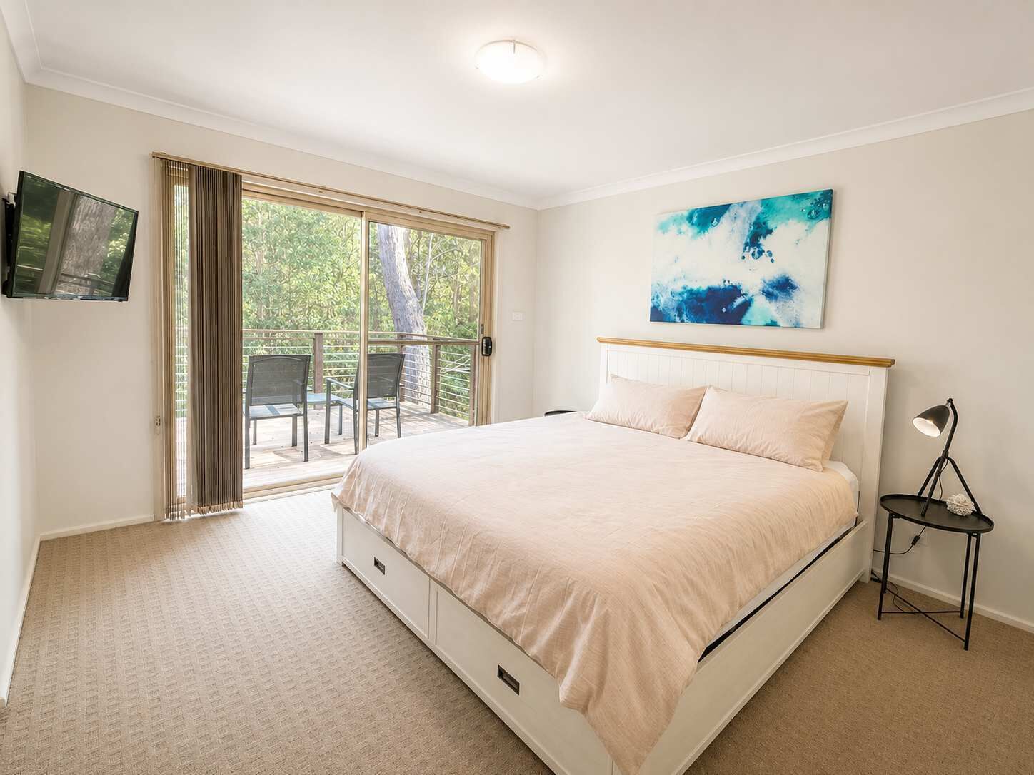 A bedroom with a bed, a television, a painting, and a balcony.
