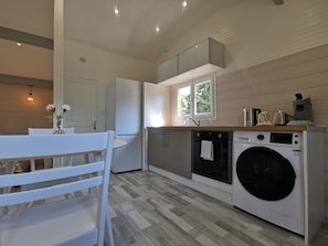 A modern kitchen with a built-in washing machine, a dining area with a white table and chairs, and a window providing natural light. - ? Chalet 10 Min. DE Reims (Prouilly)