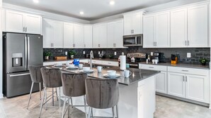 Una cocina moderna con armarios blancos, electrodomésticos de acero inoxidable y una isla central con taburetes de bar.