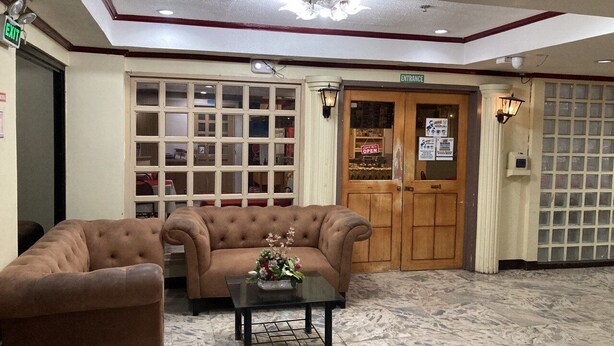 A lobby with two sofas, a coffee table, and a reception area with a wooden door and glass panels. - Demiren Hotel and Restaurant (Cagayan de Oro)