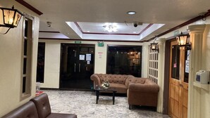 A lobby with a brown leather sofa, a matching armchair, a coffee table with a floral arrangement, and a marble floor. There are two exits marked with green signs. - Demiren Hotel and Restaurant (Cagayan de Oro)