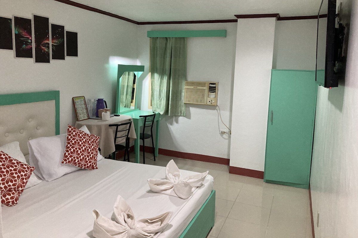A hotel room with a bed, a desk, a chair, a television, and a wardrobe.