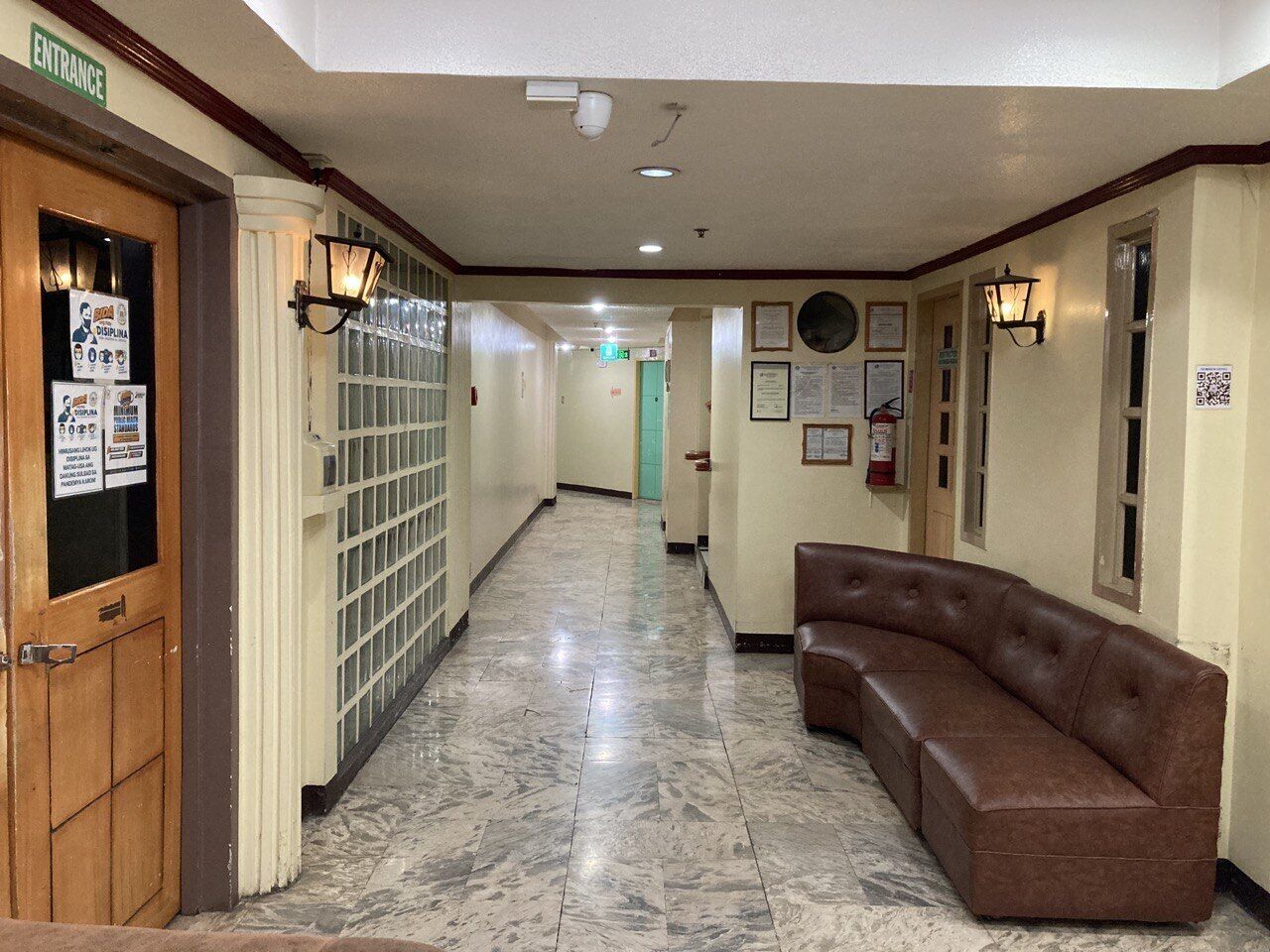 A hotel lobby with a marble floor, a brown leather sofa, and a wooden door labeled "ENTRANCE".