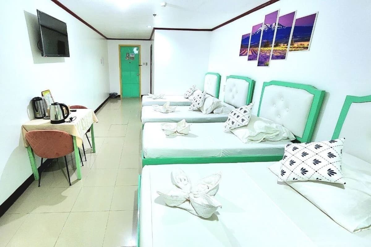 A hotel room with four beds, a desk with a chair, a television, and a green door.