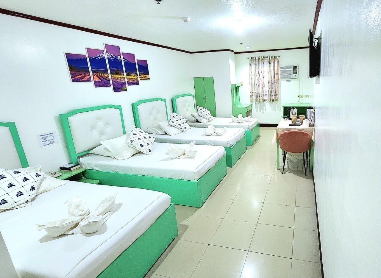 A hotel room with four beds, a desk, and a chair.