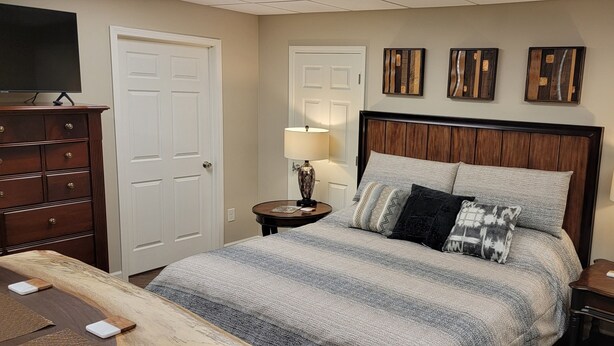A bedroom with a large bed, two bedside tables with lamps, a dresser, and a television on a stand. - Apartment at the base of the Blue Ridge Mountains (Lenoir)