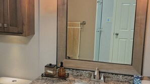 A bathroom with a granite countertop sink, wooden cabinets, a large mirror, and a hanging light fixture. - Apartment at the base of the Blue Ridge Mountains (Lenoir)