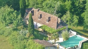 An aerial view of a house with a swimming pool surrounded by lush greenery.