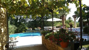An outdoor pool area with a stone wall, potted plants, and outdoor furniture.