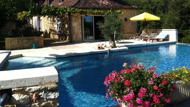 A pool area with a stone house, a yellow umbrella, and a flower bed.