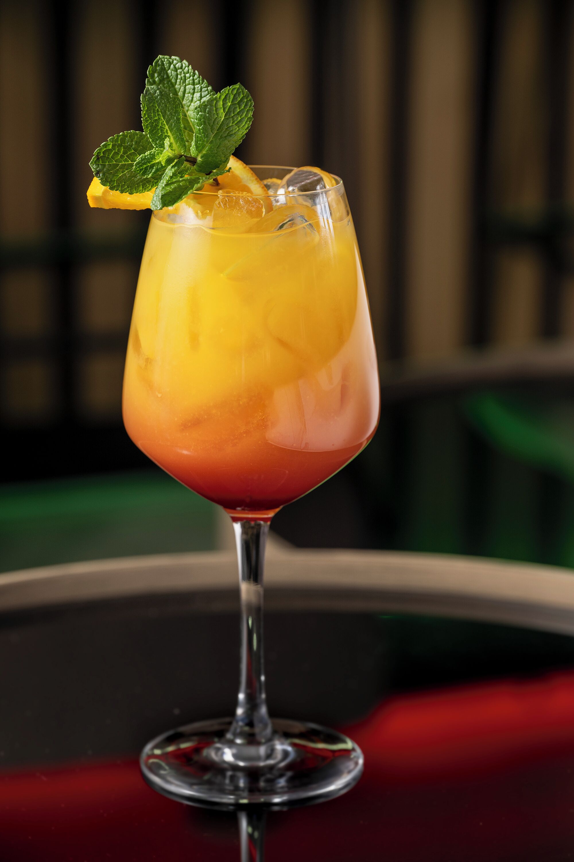 Un verre à cocktail, agrémenté d’un fruit, posé sur une surface réfléchissante.