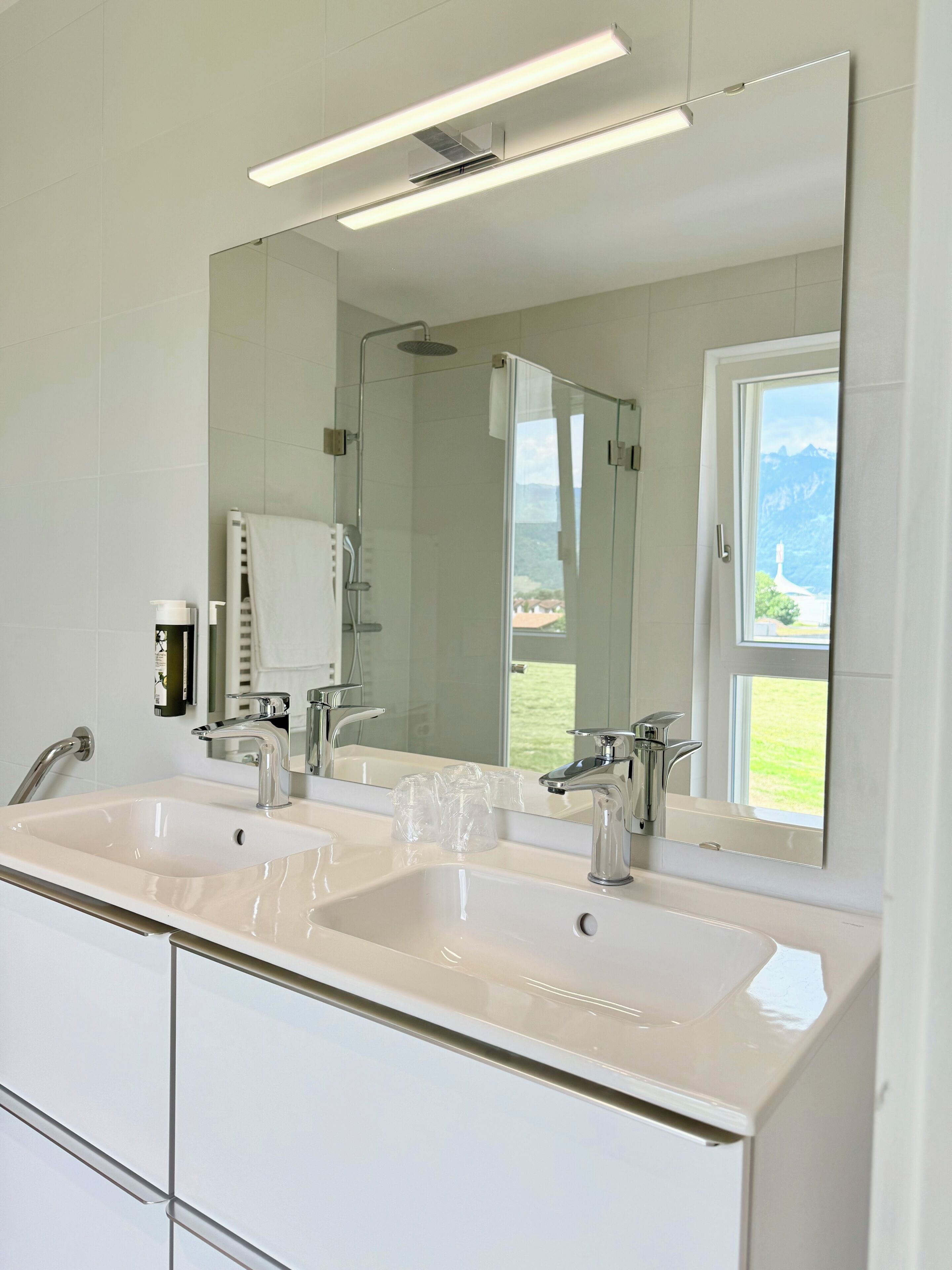 A modern bathroom with two sinks, a large mirror, and a shower.