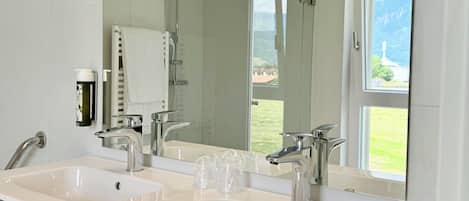 A modern bathroom with two sinks, a large mirror, and a shower.