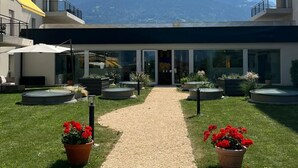 A hotel entrance with a gravel path leading to the door, surrounded by potted plants and a mountain view. - Alparthotel  (Collombey-Muraz)