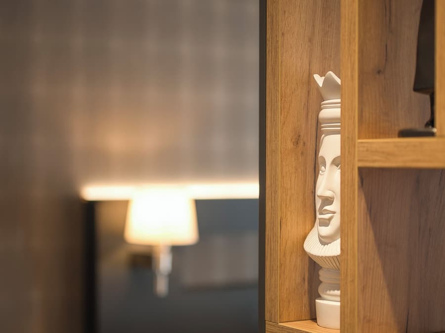 Un separador de madera con una escultura de busto blanco, una lámpara de noche y una cama al fondo.