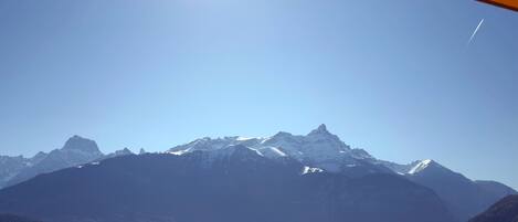 Cordillera montañosa con picos nevados, cielo despejado y una vista distante de un pueblo con edificios y árboles.