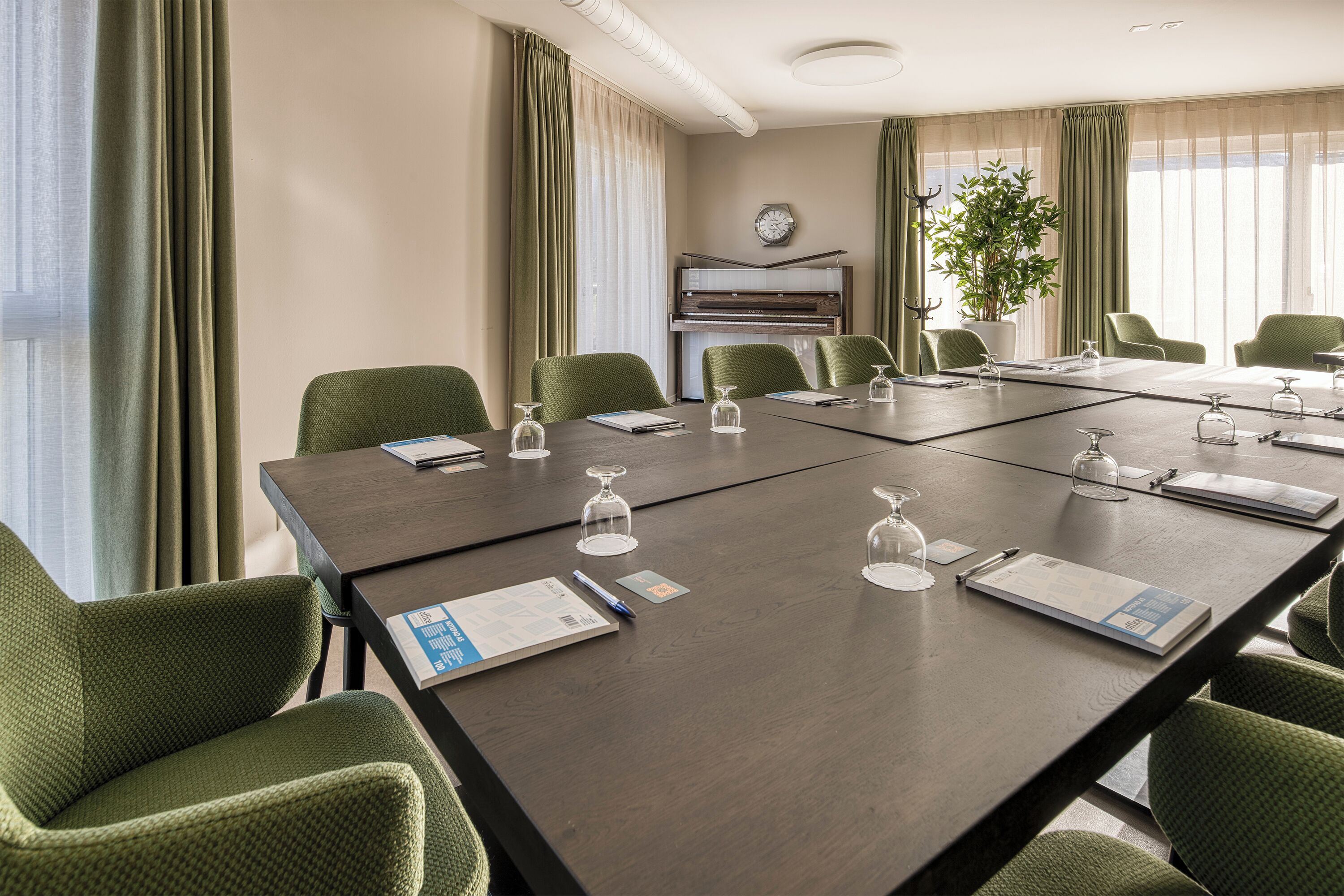 A conference room with a long table, green chairs, a piano, and a clock on the wall.