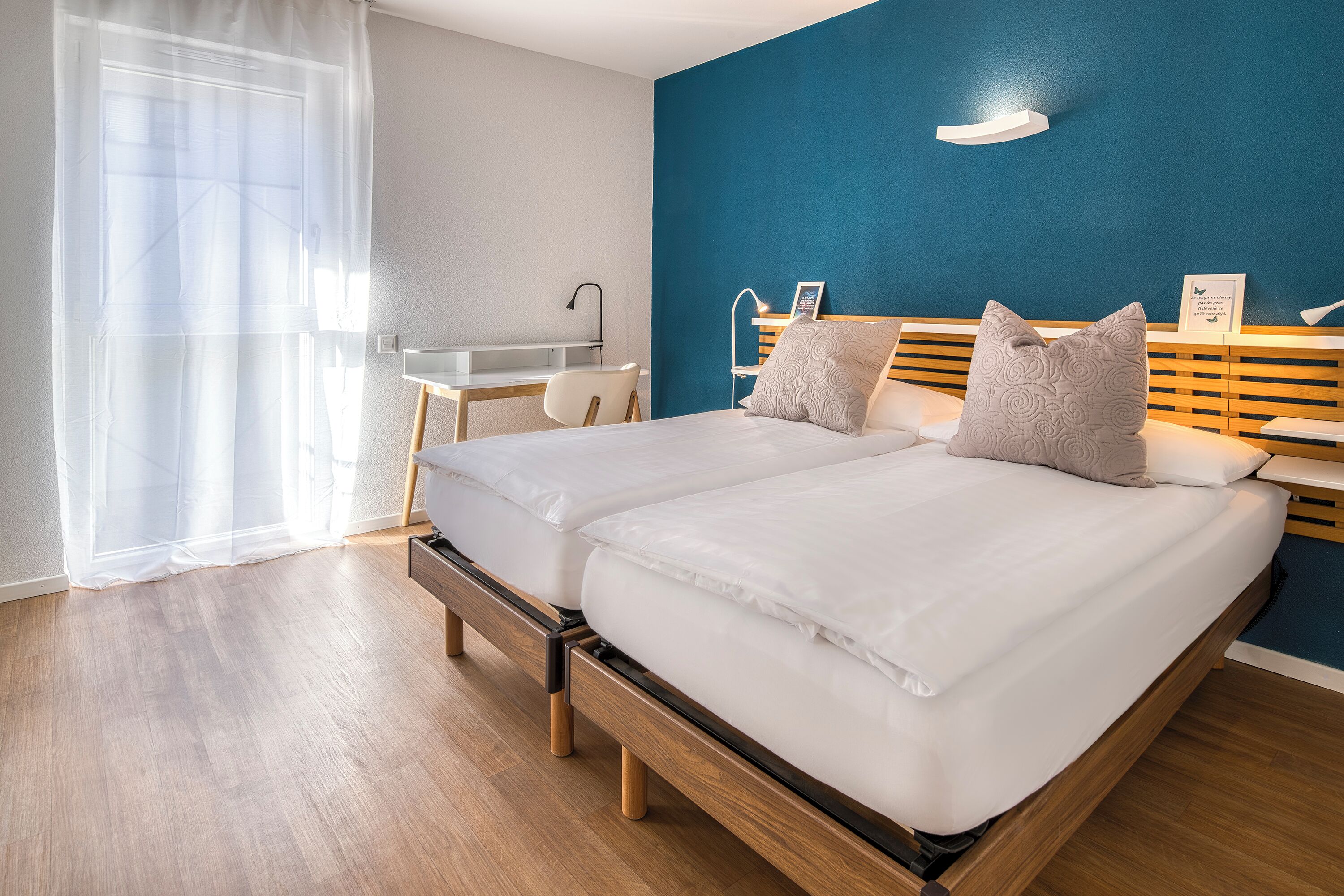 A double bed with a wooden frame, a desk with a chair, and a blue accent wall.