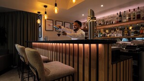 A bar area with a bartender, bar stools, and a variety of liquor bottles. - Alparthotel  (Collombey-Muraz)