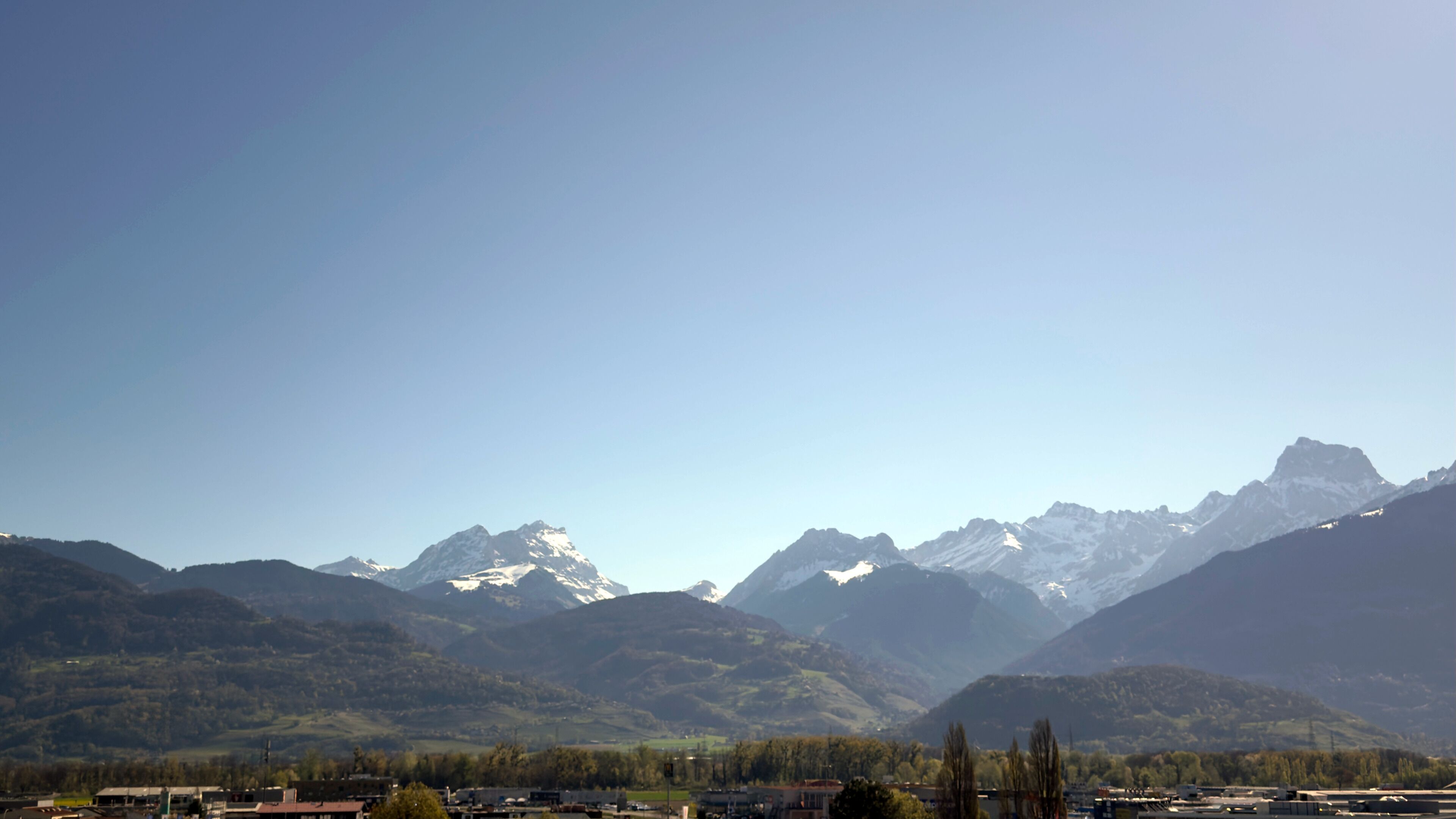 A mountainous landscape with snow-capped peaks and a valley with buildings.