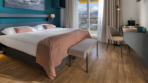 A hotel room with a bed, a desk, a chair, a large window with a mountain view, and a painting on the wall. - Alparthotel  (Collombey-Muraz)