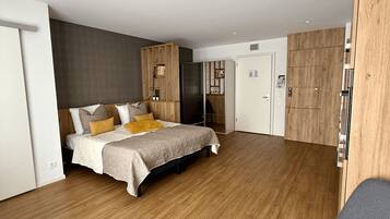 Ein modernes Schlafzimmer mit Holzboden, einem Bett mit gemustertem Überwurf, einem Schreibtisch mit Stuhl und einem Kleiderschrank.