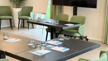 A conference room with a large table, green chairs, a flat-screen TV, a whiteboard, and a potted plant.