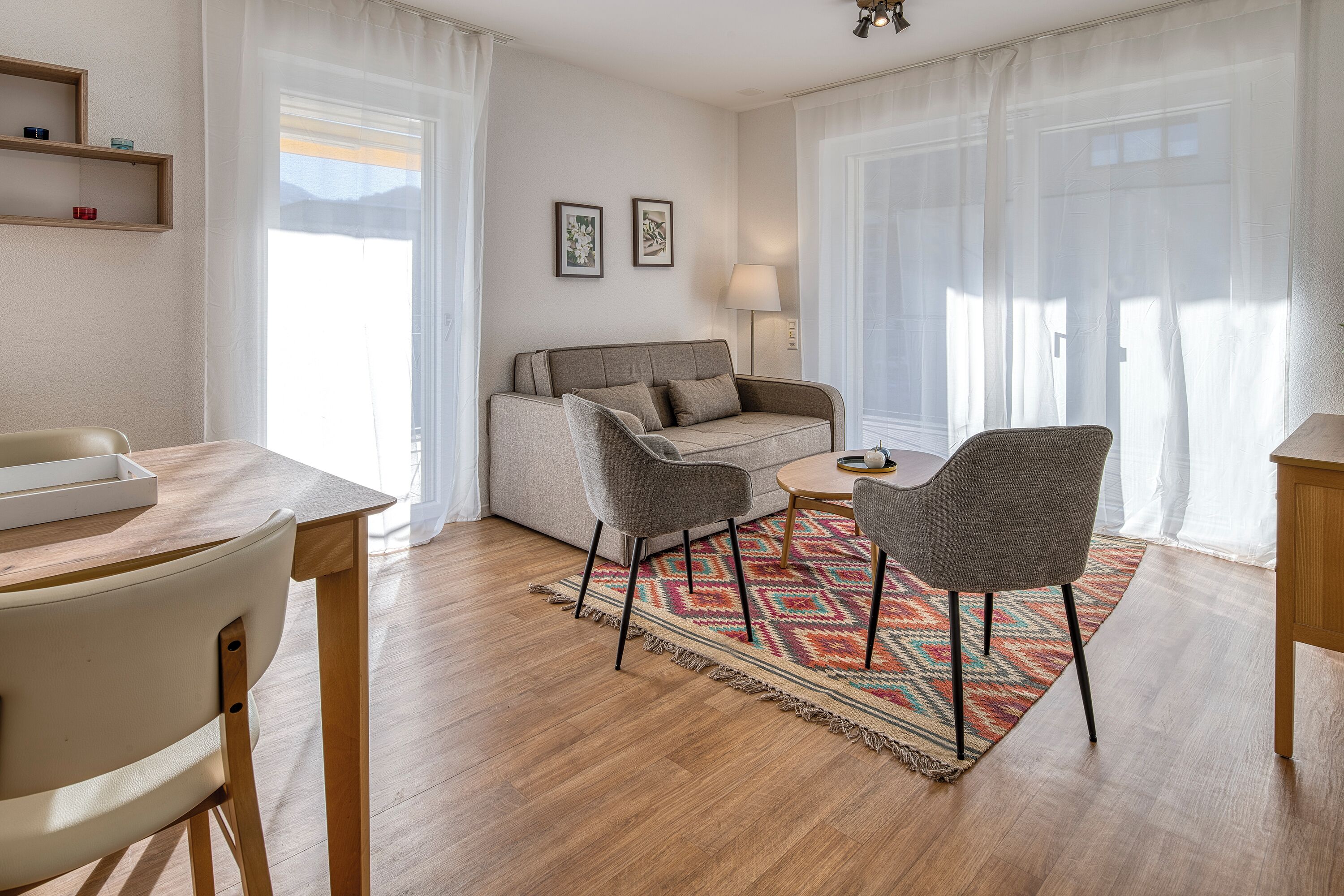 A modern living room with a sofa, two armchairs, a small round table, and a wooden floor.