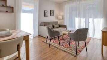 A modern living room with a sofa, two armchairs, a small round table, and a wooden floor.