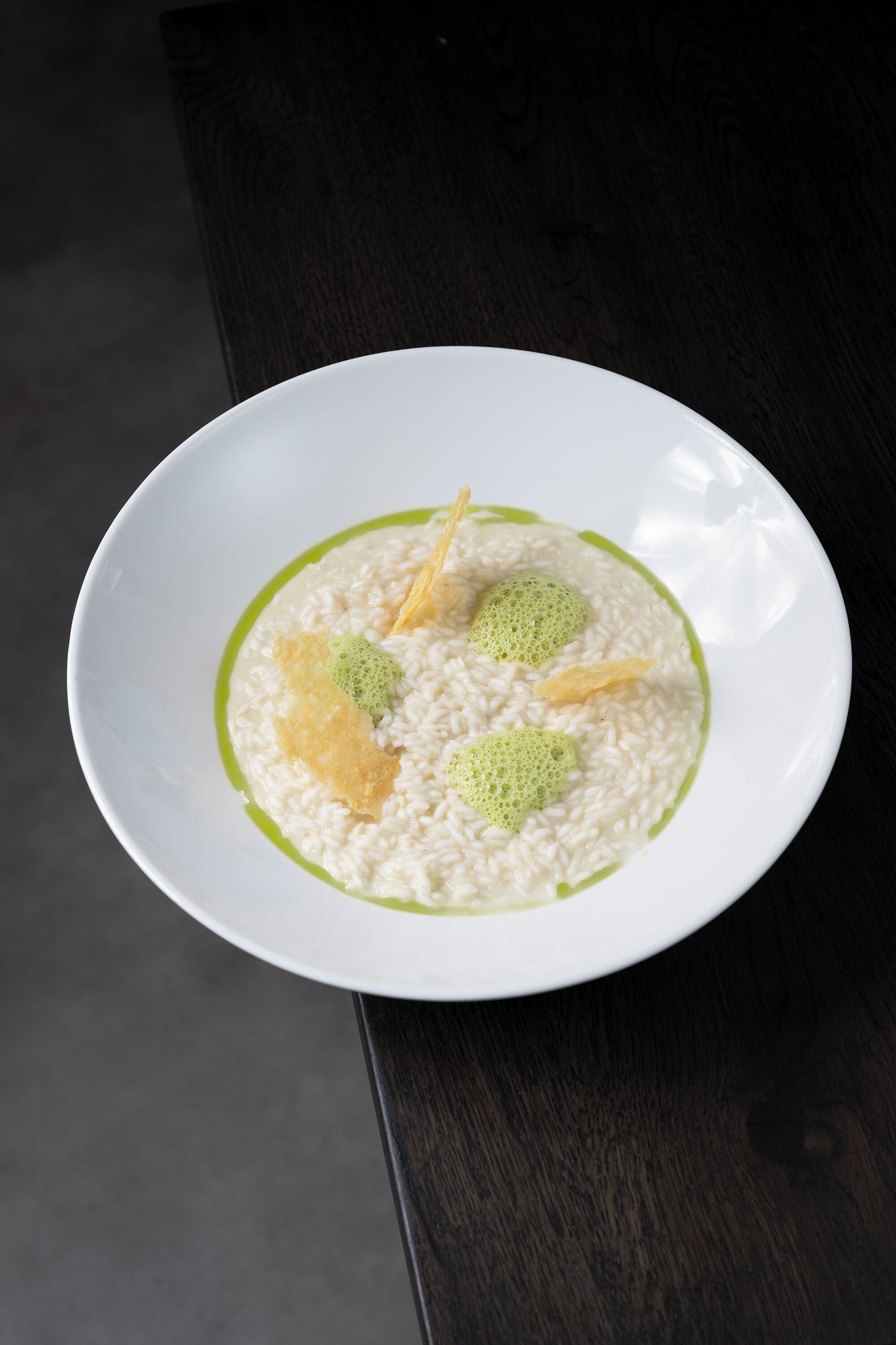 Un plato blanco con arroz y guarnición verde sobre una superficie oscura.