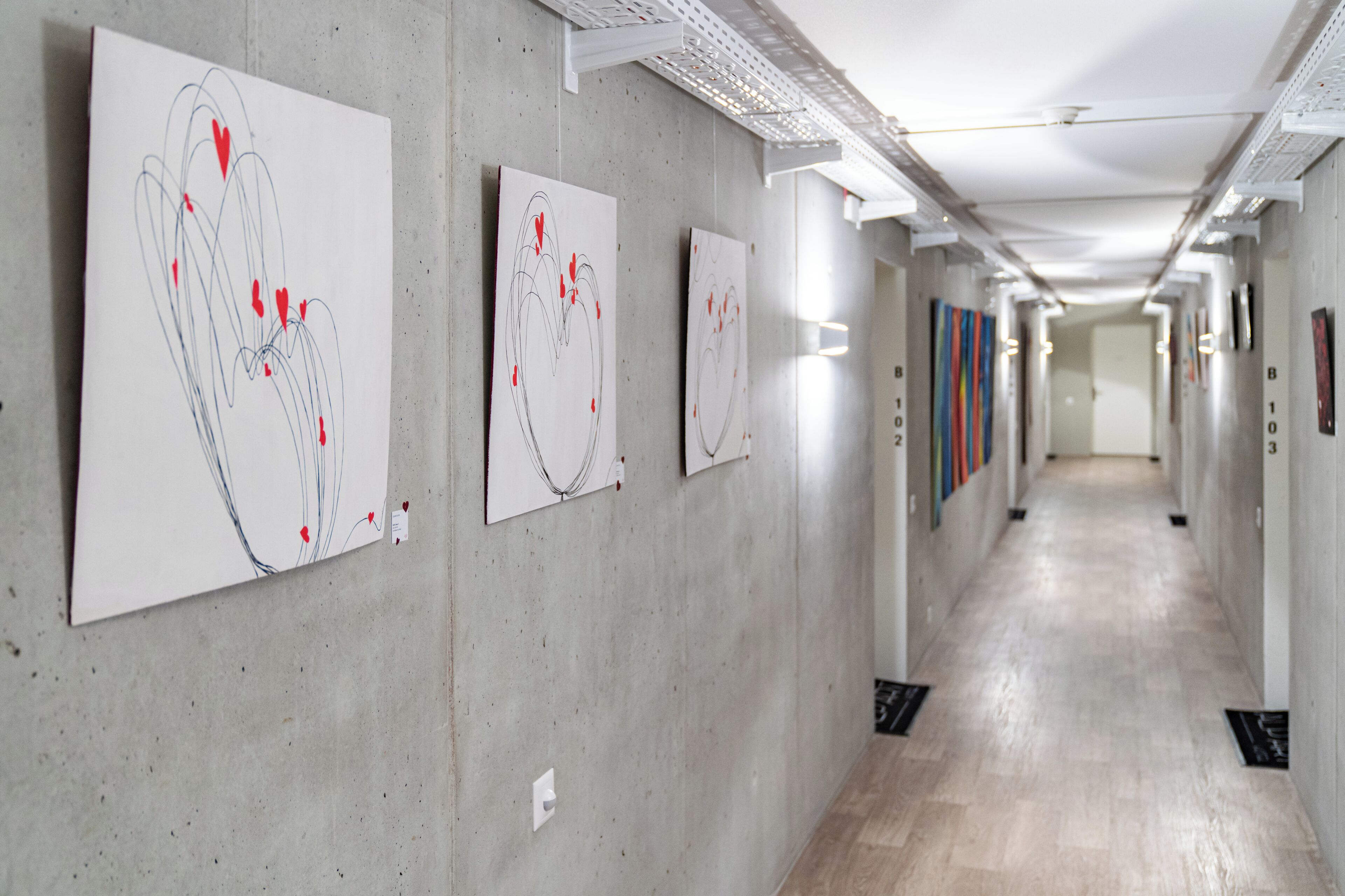 A hallway with artworks on the walls, a concrete floor, and a long corridor.
