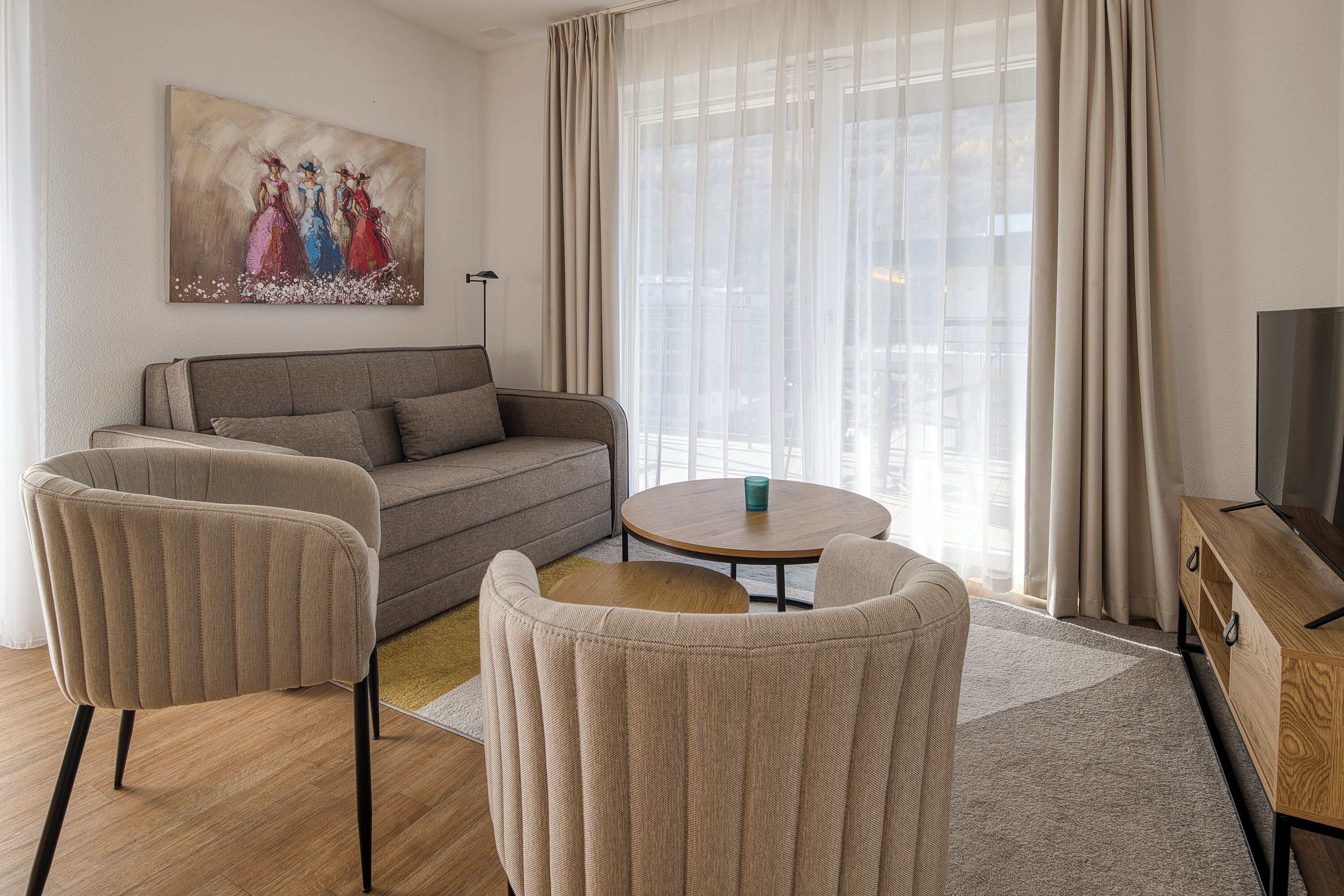 Ein Wohnzimmer mit einer Couch, zwei Sesseln, einem Couchtisch, einer TV-Konsole und einem Bild an der Wand.