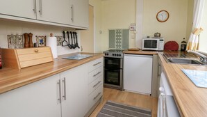 A compact kitchen with white cabinets, a microwave, a stove, and a sink. - Llwynon (Aberystwyth)