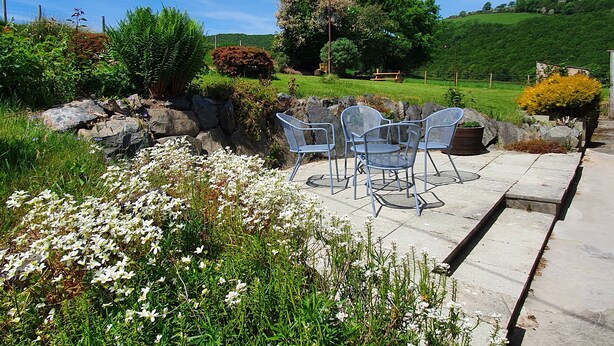A patio area with outdoor seating and a view of a green landscape. - Llwynon (Aberystwyth)