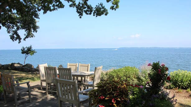 Une terrasse avec des chaises et une table en bois, donnant sur une étendue d’eau.