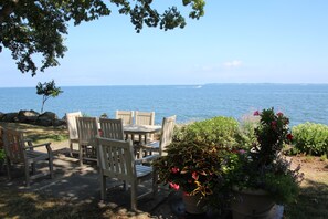 A patio with wooden chairs and a table overlooking a body of water.