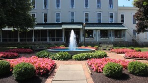 Un bâtiment avec une fontaine au centre, entouré de parterres de fleurs et d’un chemin pavé.